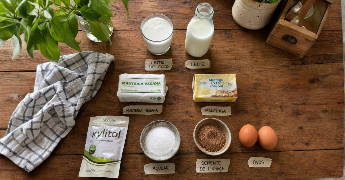 Bolo de Maisena: A Receita Clássica que a Vovó Fazia! 3 Flat lay com ingredientes substitutos para bolo de maisena sobre bancada rústica, incluindo leite de coco, manteiga vegetal, linhaça e xilitol lado a lado