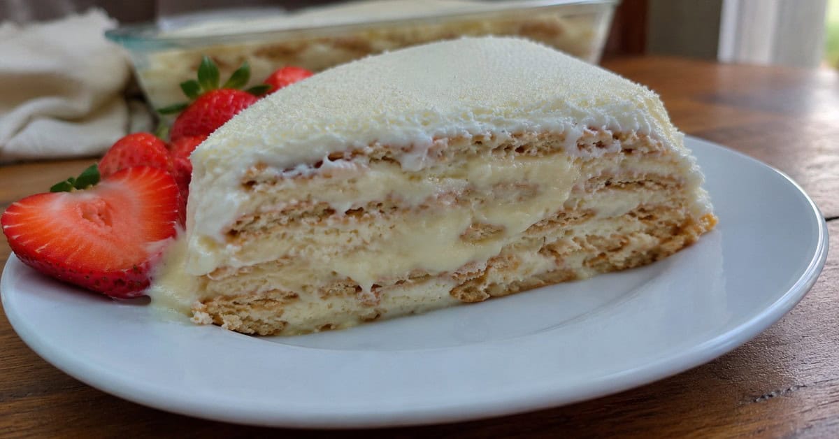 Torta Alemã de Leite Ninho 1 Fatia de torta alemã de leite ninho em prato branco com morangos e polvilhado de leite em pó