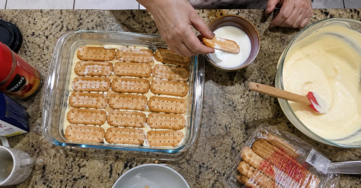 Torta Alemã de Leite Ninho 2 Mãos montando a torta alemã de leite ninho em refratário com camadas de biscoito e creme branco