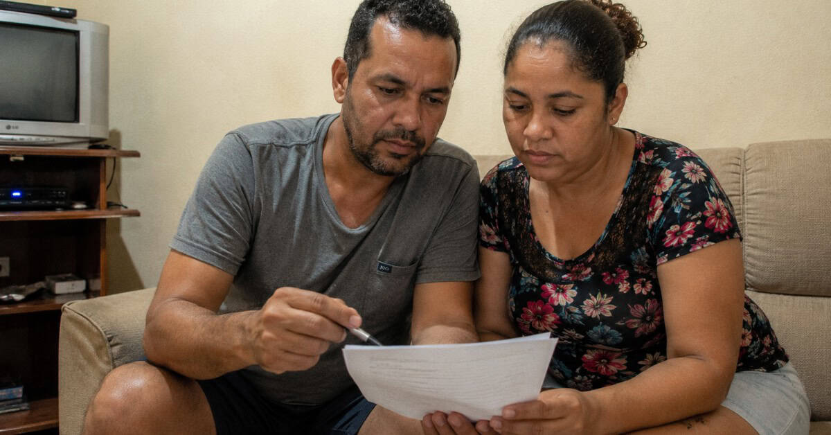 Como Conseguir uma Casa na Minha Casa Minha Vida 6 Casal sentado no sofá analisando contrato de financiamento habitacional antes de assinar pelo programa Minha Casa Minha Vida