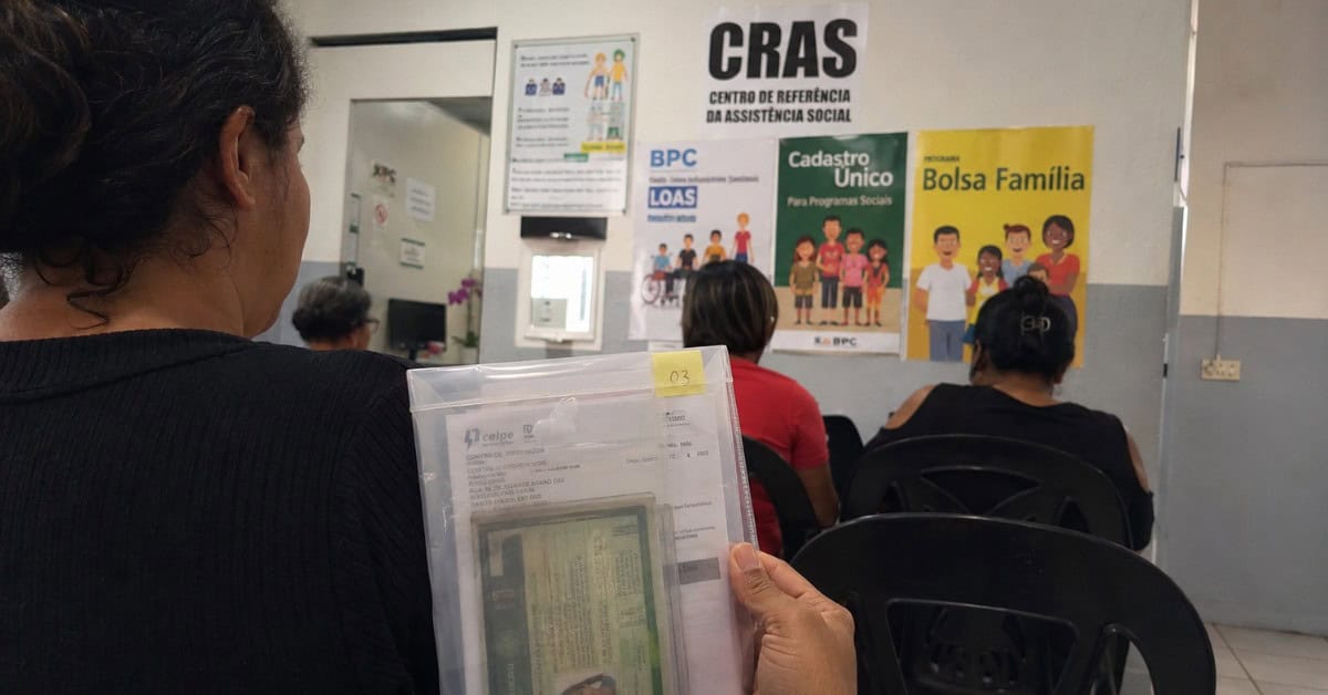 O Gás de Cozinha que Pesava no Bolso — e a Solução que Virou Lei 4 Mulher de costas na fila do CRAS segurando pasta transparente com documentos pessoais como RG e comprovante de residência para cadastro no CadÚnico