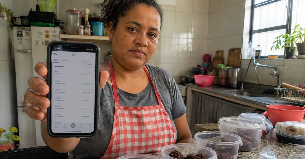 Como Conseguir uma Casa na Minha Casa Minha Vida 4 Mulher empreendedora em cozinha caseira mostrando extrato bancário no celular como comprovante de renda para o Minha Casa Minha Vida