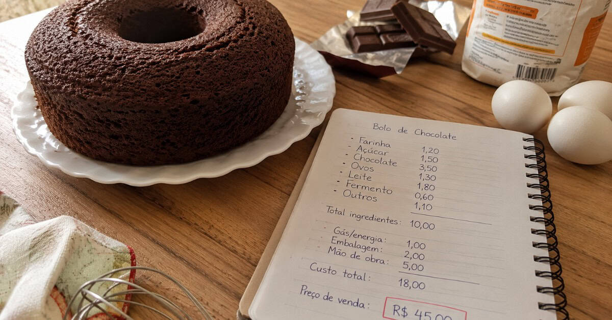 Como Fazer 5 Mil Reais Vendendo Bolo: O Guia Honesto para Transformar Sua Cozinha em Negócio 3 Bolo de chocolate caseiro sobre prato branco com caderno de custos aberto, ovos e barra de chocolate ao fundo, em cozinha iluminada por luz natural